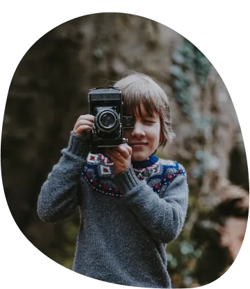 Bambino con un maglione grigio scatta una foto con una macchina fotografica d'epoca