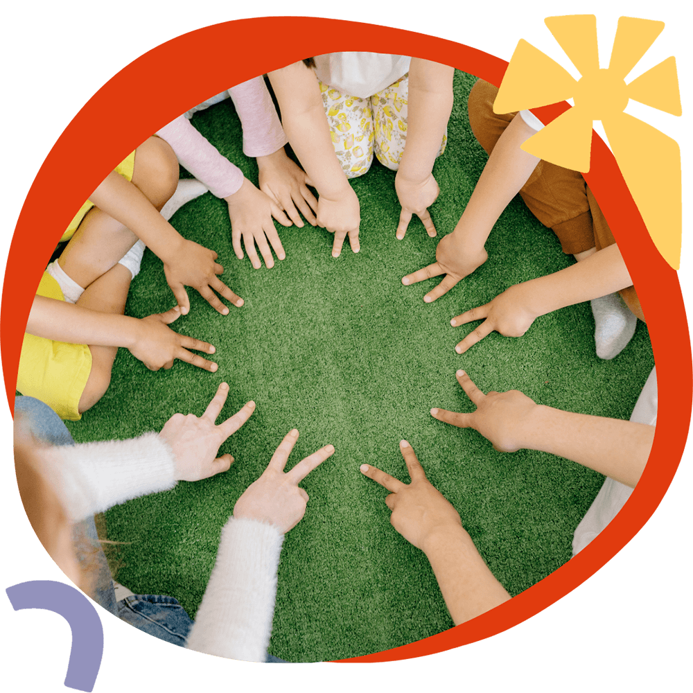 Un gruppo di bambini seduti in cerchio sull'erba con le mani al centro, durante un'attività CLIL del corso estivo Move Your Summer